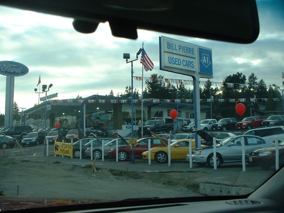 Bill Pierre Used Cars dealership lot with multiple vehicles under a cloudy sky