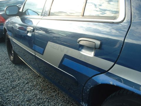 1999 Ford Crown Victoria - Side view of a blue sedan with a graphic stripe. Another vehicle is visible in the background.