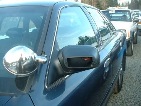1999 Ford Crown Victoria - A dark blue sedan is parked in a line with other vehicles. The passenger side mirror is missing.