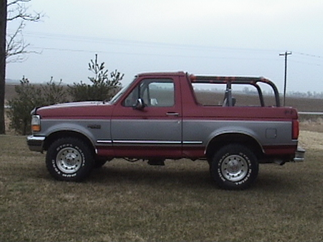 Side view of a red and gray Ford Bronco parked on grass. It has a roll bar in the back