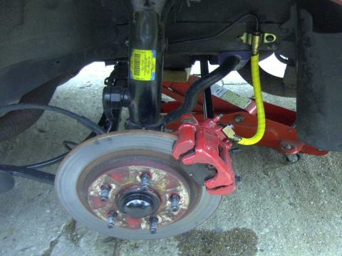 1997 Ford Taurus - Close-up view of a red rear brake caliper and rotor assembly, with a yellow brake line visible.