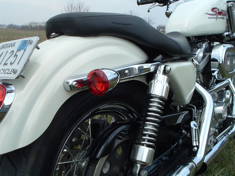 White motorcycle rear fender with Indiana license plate and red taillight. Chrome accents and black seat visible