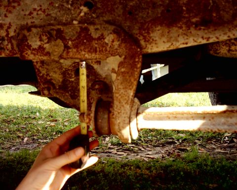 1978 Ford Bronco - Close-up of a heavily rusted vehicle frame and suspension component, with a measuring tape indicating a dimension.