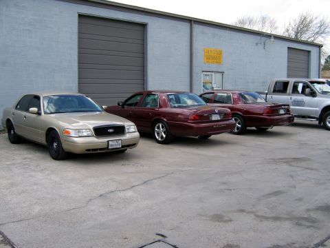2000 Ford Crown Victoria - A gold 2000 Ford Crown Victoria is parked in front of a building alongside two other sedans and a pickup truck.
