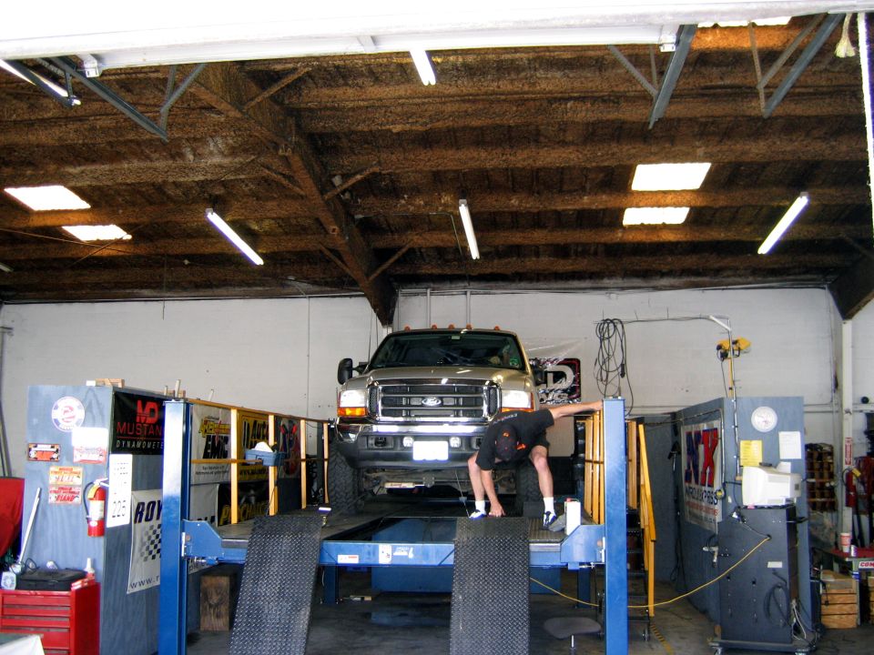 Ford F-Series truck on a lift in a garage with a person bending over near the front wheel