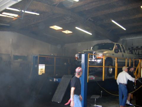 2000 Ford Crown Victoria - A silver pickup truck is positioned on a dynamometer lift inside a workshop, with several people observing.