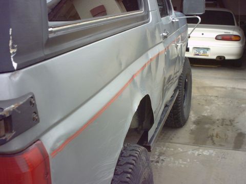1990 Ford Bronco - The side of a silver Ford Bronco is shown, with a white car parked behind it in a garage.