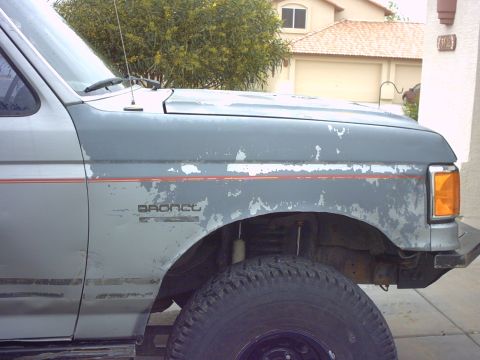 1990 Ford Bronco - The fender and hood of a 1990 Ford Bronco show significant paint wear and a red stripe detail.
