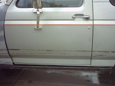 1990 Ford Bronco - Side view of a silver SUV door, showing chrome trim and orange pinstripes along the body.