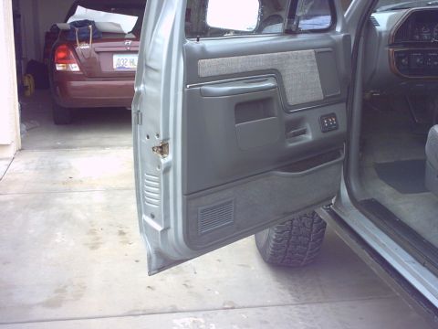 1990 Ford Bronco - The interior door panel of a 1990 Ford Bronco is visible, with a glimpse of the exterior and another vehicle in the background.