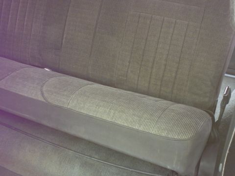 1990 Ford Bronco - The interior of a vehicle shows a gray fabric bench seat with dark gray vinyl trim.