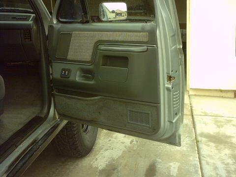1990 Ford Bronco - Interior view of a gray door panel with fabric accents and visible controls.