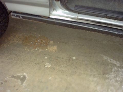 1990 Ford Bronco - The image shows the lower part of a vehicle's side, including the door, running board, and a tire, resting on a stained concrete surface.