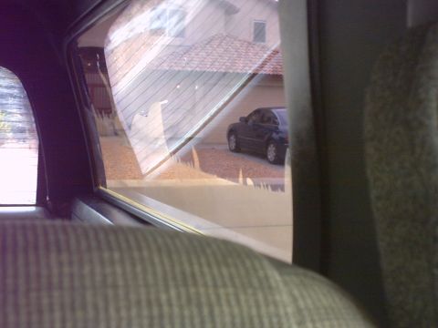 1990 Ford Bronco - A dark sedan is parked in a driveway, viewed through the window of another vehicle.