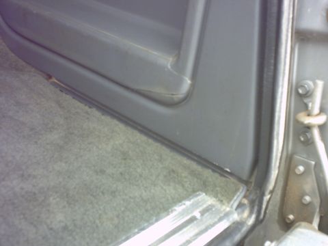 1990 Ford Bronco - Interior shot showing the door panel and carpet of a vehicle, with a visible latch mechanism.