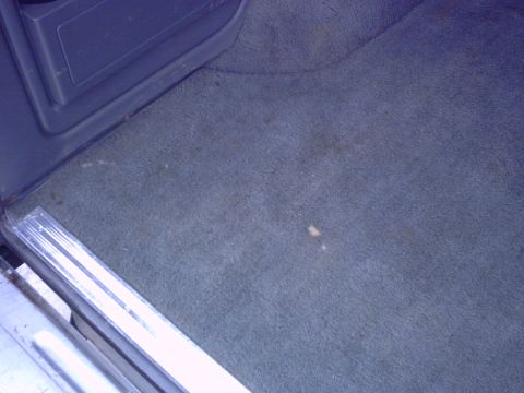 1990 Ford Bronco - Car interior carpet detail with visible stains and door sill trim.