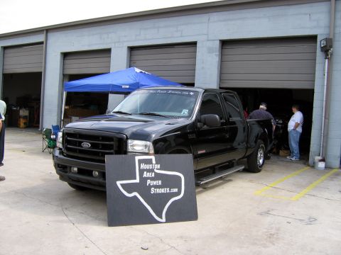 2000 Ford Crown Victoria - A black Ford F-250 Super Duty pickup truck is parked in front of a garage with a blue tent set up nearby.