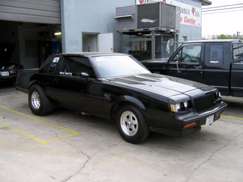 2000 Ford Crown Victoria - A black coupe with racing slicks and "NEAL WHYTE" on the door is parked next to a black pickup truck.