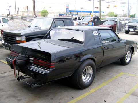 2000 Ford Crown Victoria - A black drag car with racing slicks is parked next to a black Ford pickup truck.