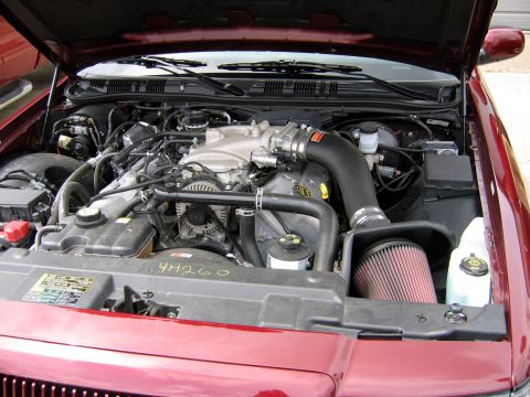 2000 Ford Crown Victoria - The engine bay of a red vehicle is shown with the hood open, revealing the motor and associated components.