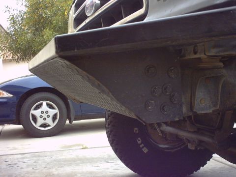 1990 Ford Bronco - The front of a truck with a custom bumper is shown, parked next to a blue sedan.