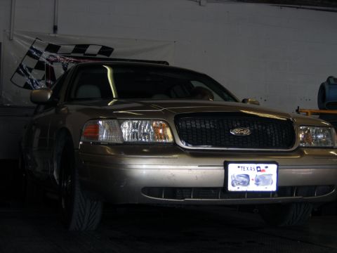 2000 Ford Crown Victoria - A gold 2000 Ford Crown Victoria is parked indoors, with a checkered flag banner in the background.