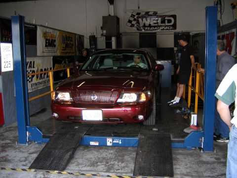 2000 Ford Crown Victoria - A Mercury Grand Marquis is positioned on a vehicle lift inside a garage, with several people observing.