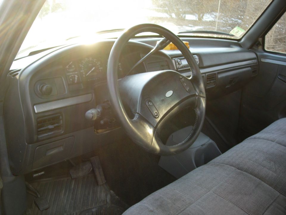 Interior of older Ford truck showing dash, gauge cluster, and Ford-emblem steering wheel