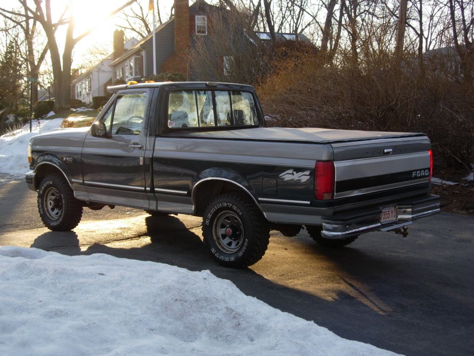 Two-tone gray and green Ford F-150 4x4 pickup with tonneau cover, rear three-quarter view on snowy driveway
