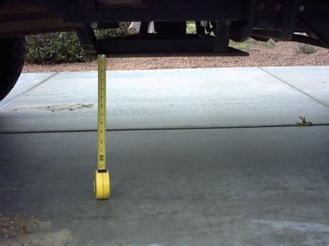 1990 Ford Bronco - A yellow measuring tape is suspended from the undercarriage of a vehicle, indicating its ground clearance.