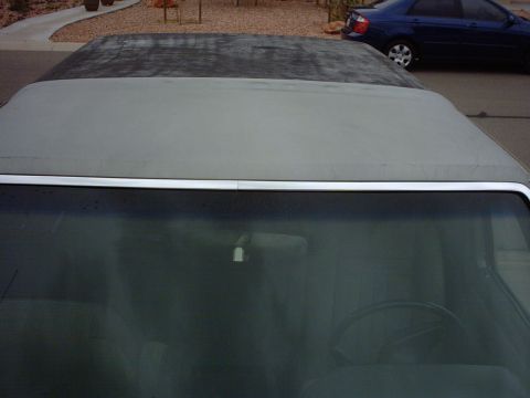 1990 Ford Bronco - A view from inside a convertible, looking out over the windshield at the soft top and a blue car in the background.