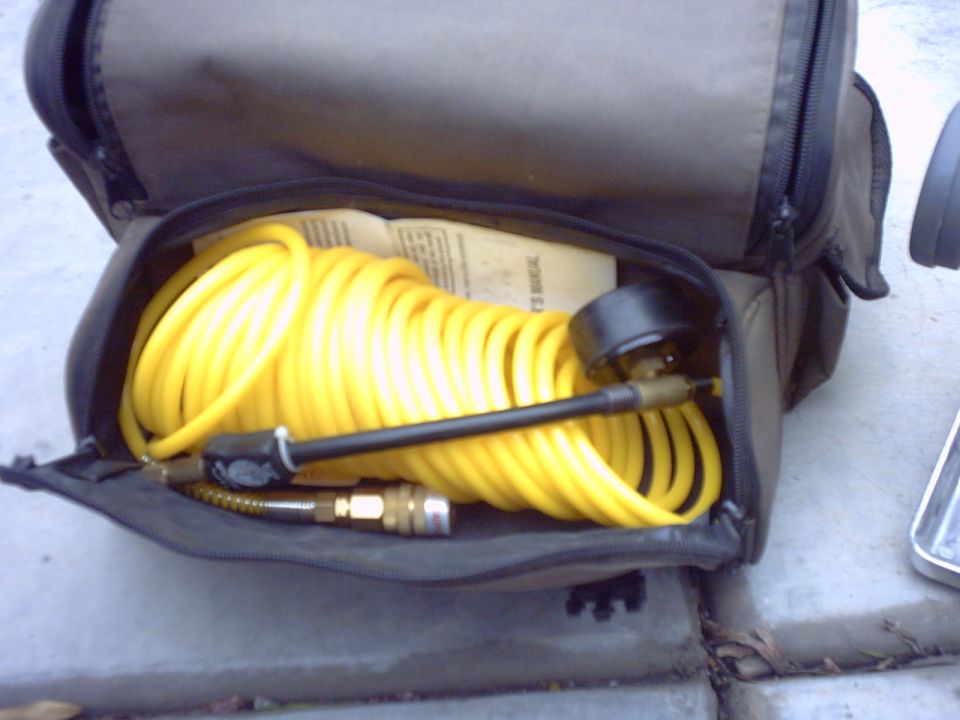 Yellow air compressor hose and gauge inside a black storage bag. A manual is visible underneath the hose