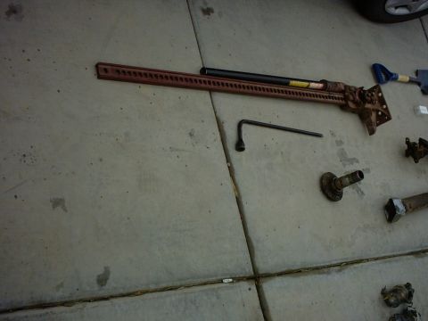 1990 Ford Bronco - Various vehicle parts, including a hi-lift jack and lug wrench, are laid out on a concrete surface.