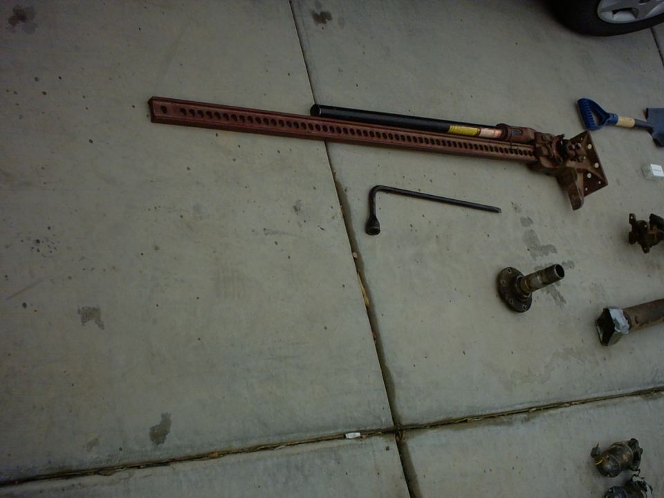 Red hi-lift jack and lug wrench on concrete, with other vehicle parts scattered nearby