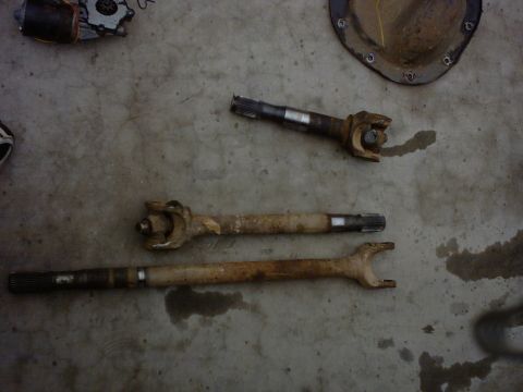 1990 Ford Bronco - Several vehicle drive shafts and a differential cover are laid out on a concrete surface.