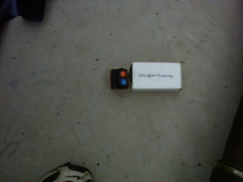 1990 Ford Bronco - A small emblem from Ford Motor Company is shown on a white box with two colored lights.