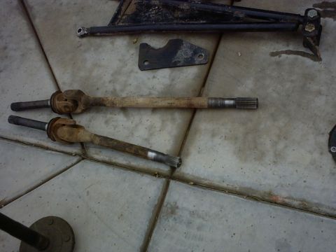 1990 Ford Bronco - Various automotive parts, including drive shafts and suspension components, are laid out on a concrete floor.