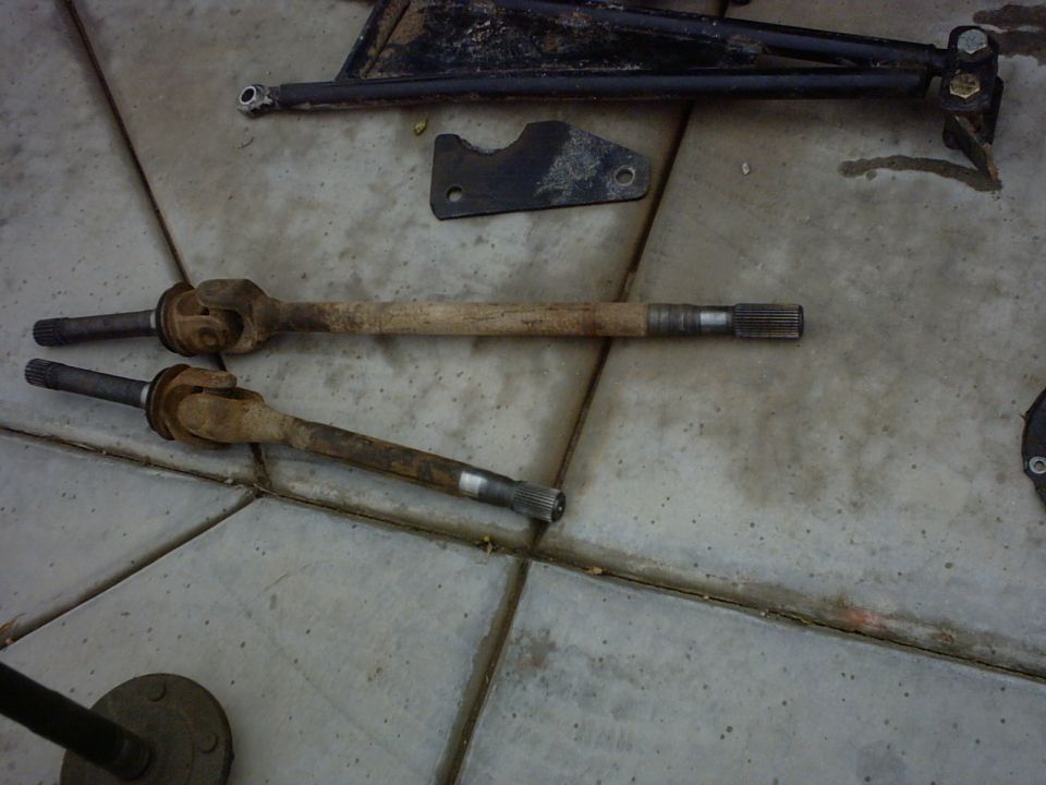 Two rusty drive shafts and black metal suspension components on a tiled floor