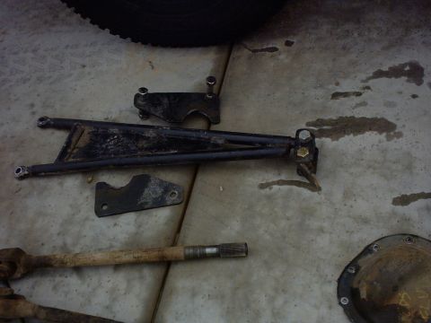 1990 Ford Bronco - Various automotive parts, including a control arm and axle shaft, laid out on a concrete surface.