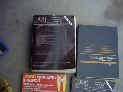 1990 Ford Bronco - A collection of vehicle shop manuals, including one for a 1990 Ford Bronco, is laid out on a concrete surface.