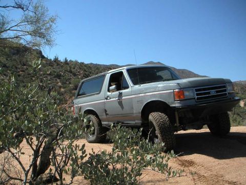 1990 Ford Bronco - Ford Bronco navigating a dusty off-road path under a clear blue sky.