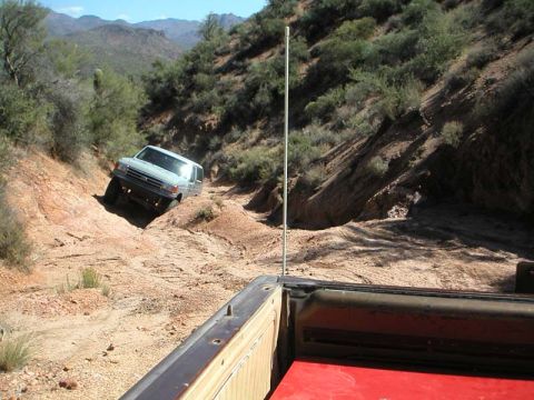 1990 Ford Bronco - A Ford Bronco navigates a challenging off-road trail in a desert landscape.