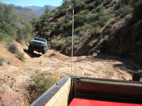 1990 Ford Bronco - A Ford Bronco navigates a steep, dusty trail in a mountainous desert landscape.