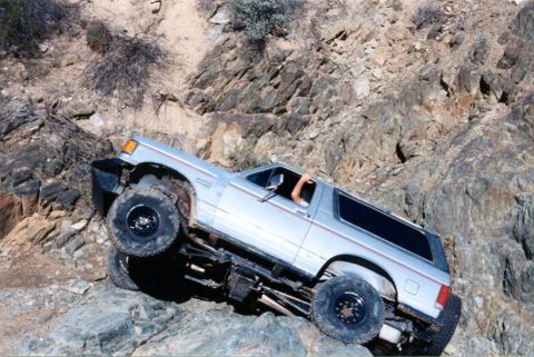 1990 Ford Bronco - This silver SUV is tackling a challenging off-road trail with steep, rocky terrain.