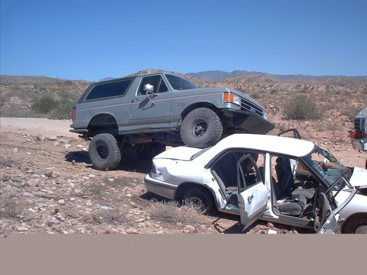 Gray 1990 Ford Bronco lifted over a white sedan