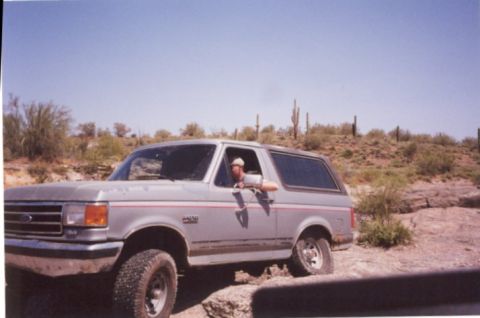 1990 Ford Bronco - A silver Ford Bronco is parked on a rocky desert trail under a clear blue sky.