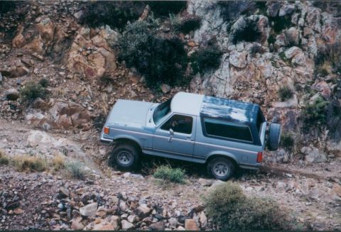 1990 Ford Bronco - This SUV navigates a challenging rocky terrain, its off-road capabilities. The visible text indicates it's from SUPERMOTORS.