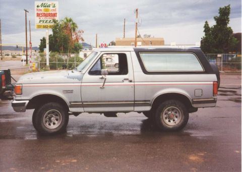 1990 Ford Bronco - Side view of a 1990 Ford Bronco parked on a wet street.