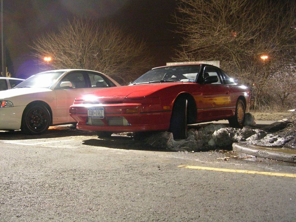 Red Nissan 240SX parked on snow with a white sedan beside it. License plate reads CUR-1962