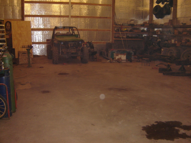 Green off-road vehicle with a roll cage parked inside a garage with shelves and other equipment